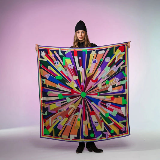 Frau mit schwarzer Mütze hält buntes Seidentuch Grand Foulard mit grafischem Muster und Schriftzug von Foulala Luzern