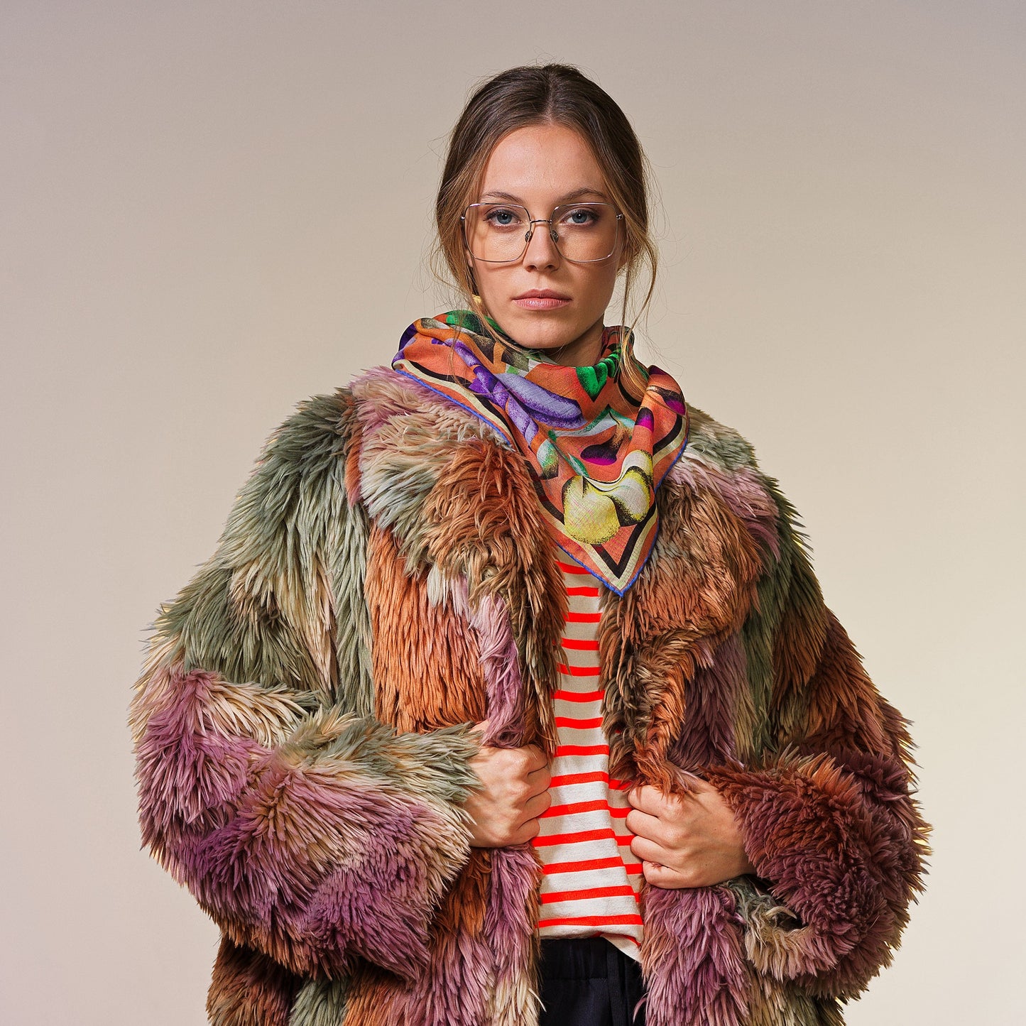 Frau mit buntem Mantel präsentiert kleines Wolltuch Foulard mit buntem Blumenmuster auf apricotfarbenem Orange Hintergrund