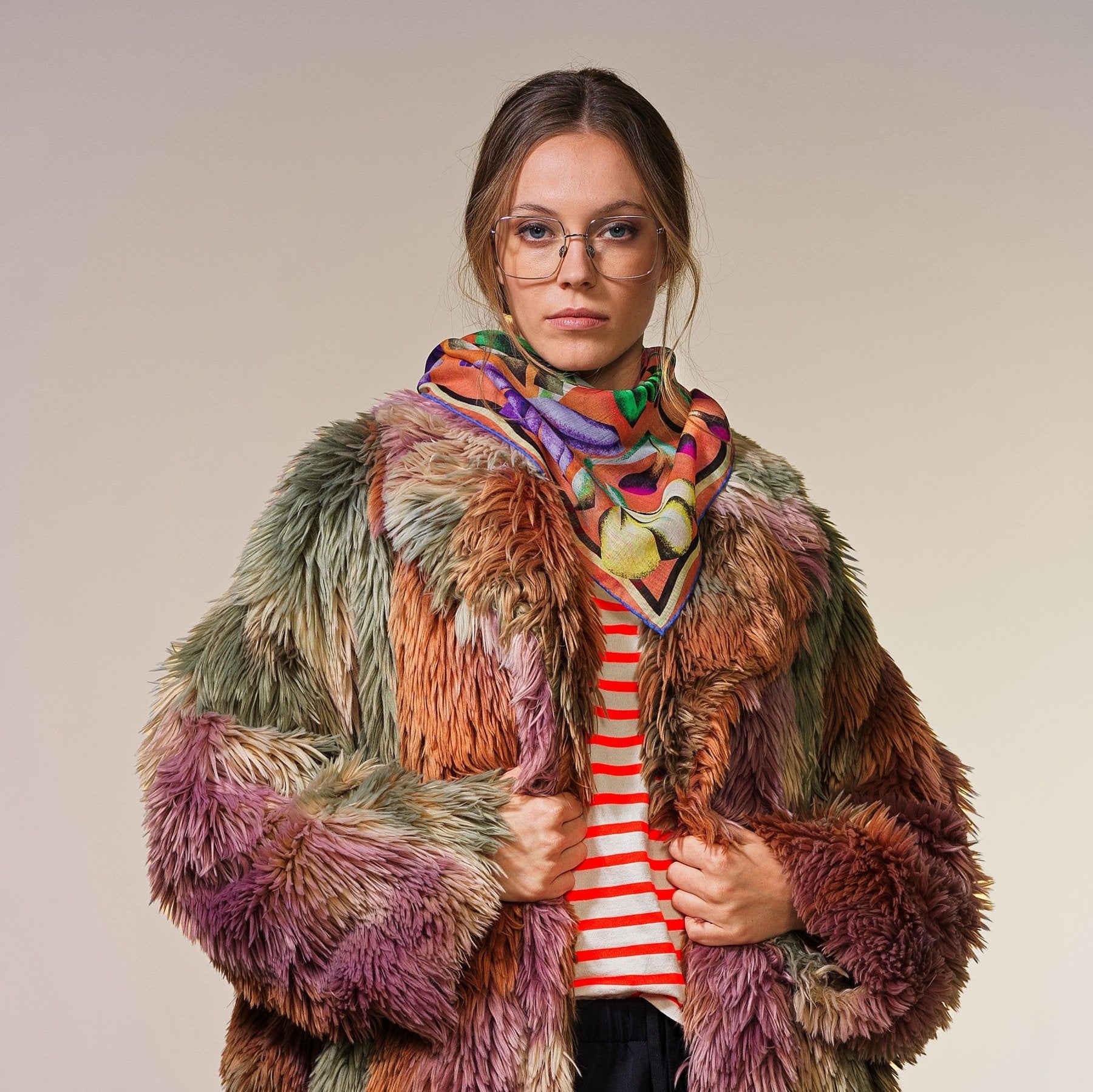 Frau mit buntem Mantel präsentiert kleines Wolltuch mit buntem Blumenmuster auf apricotfarbenem Hintergrund