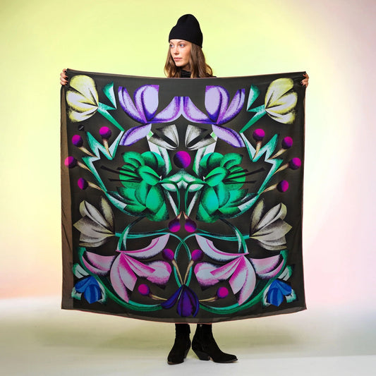 Frau mit schwarzer Mütze präsentiert grosses Tuch mit buntem, floralen Muster auf dunklem Hintergrund Damen Schweizer Design