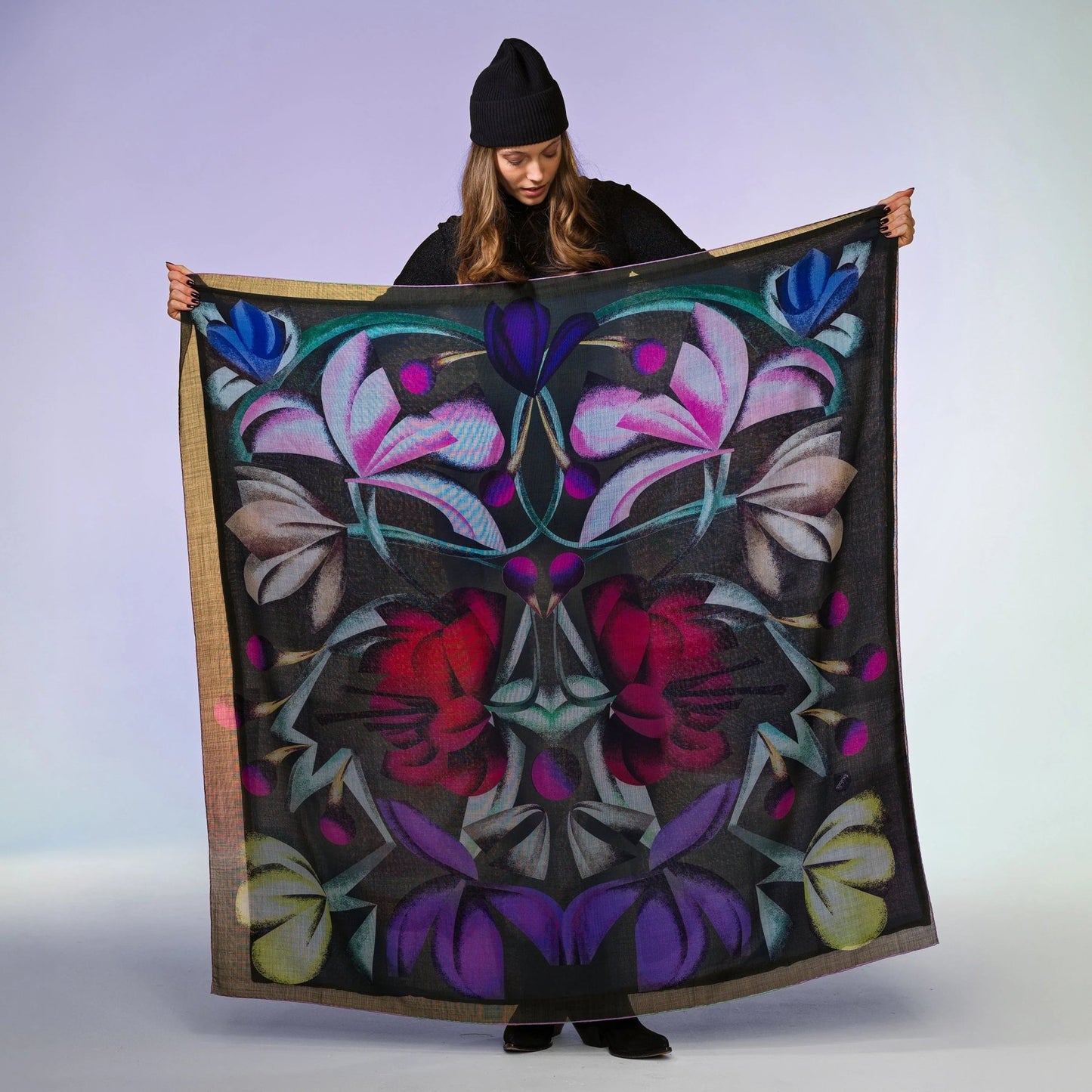 Frau mit schwarzer Mütze präsentiert großes Wolltuch mit buntem Blumenmuster auf schwarzem Hintergrund