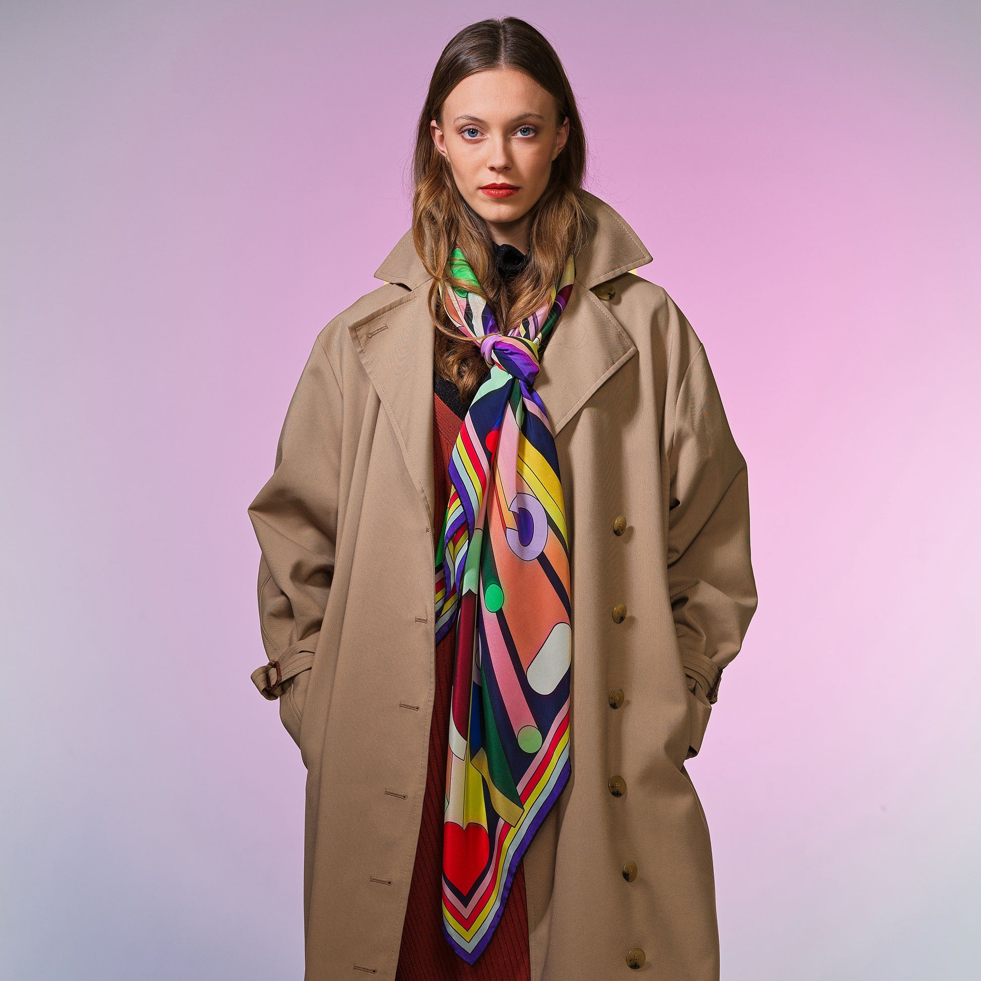Frau mit beigem Mantel trägt buntes Seidentuch mit grafischem Muster und Schriftzug