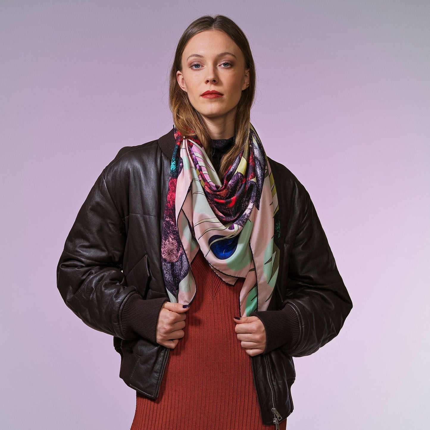 Frau mit brauner Bomberjacke trägt großes, bunt gemustertes Seidentuch vor neutralem Hintergrund von Foulala Luzern