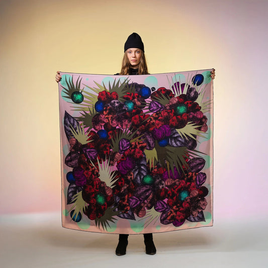 Frau mit schwarzer Mütze hält grosses, bunt gemustertes Seidentuch Foulard von Foulala vor neutralem Hintergrund